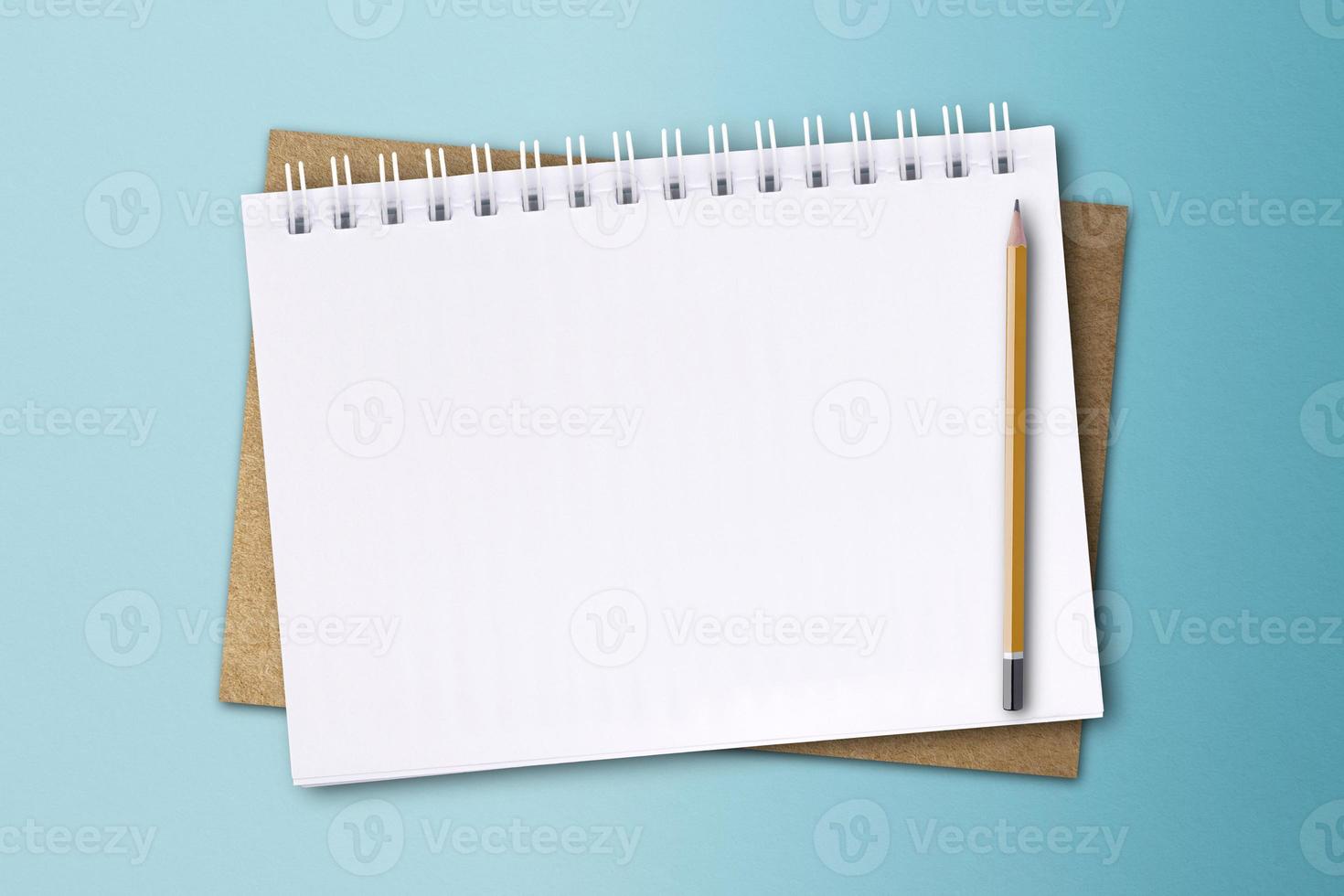 A white notebook and pencil are placed on a blue paper surface. photo