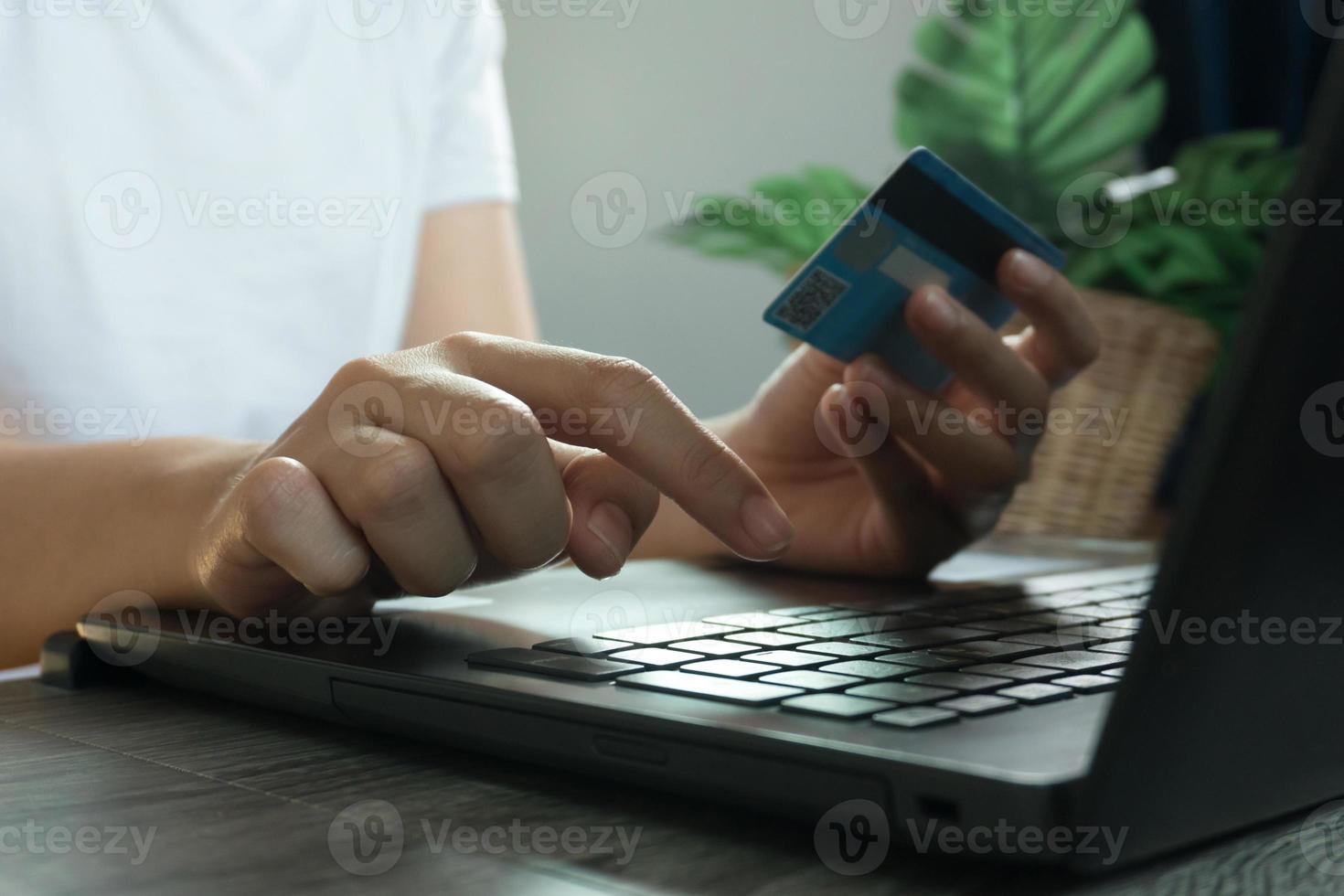 manos sosteniendo la tarjeta de crédito y usando la computadora portátil. las compras en línea. trabajo desde el concepto de casa foto