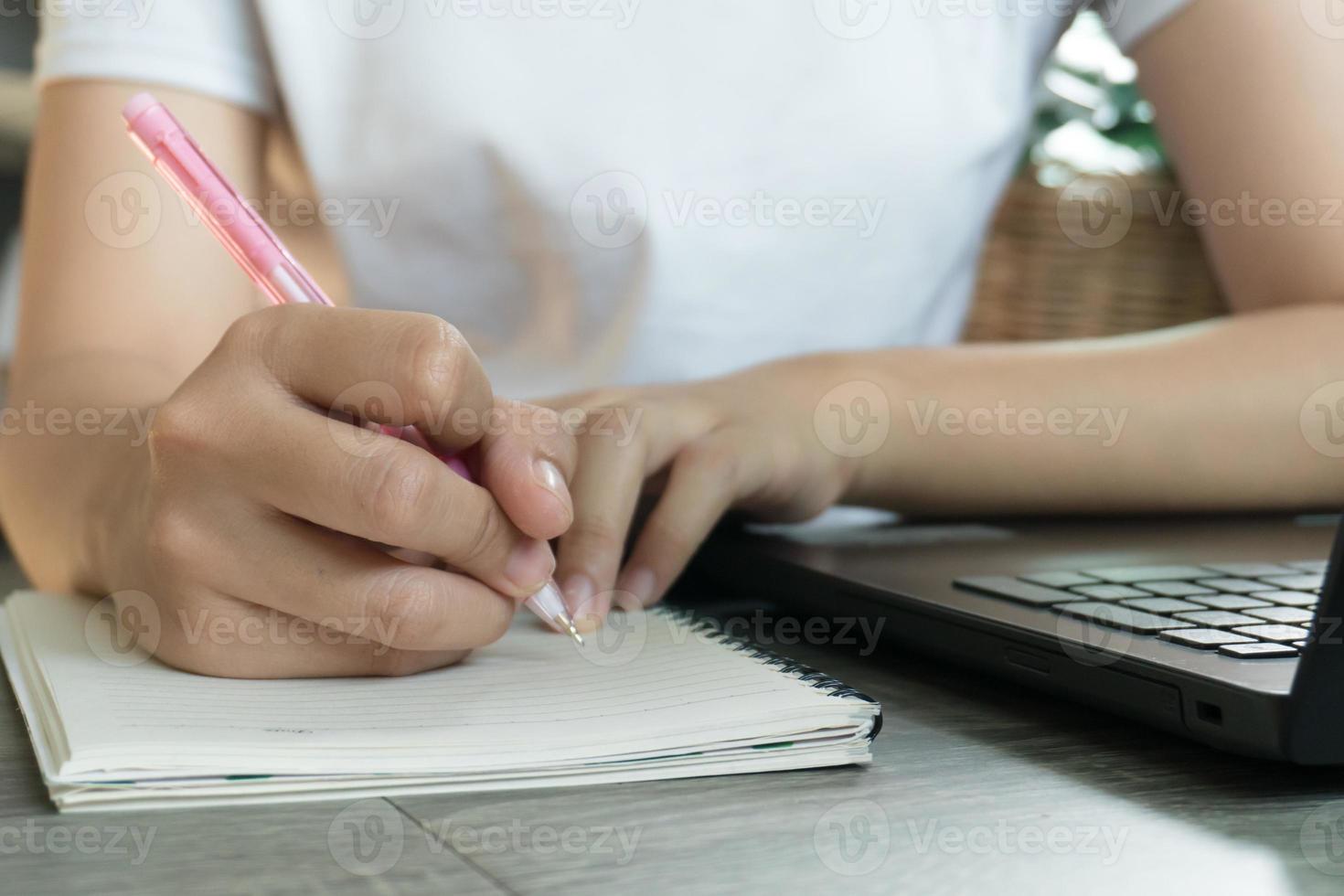 mujer de negocios joven sentada en la mesa con una computadora portátil y tomando notas en el cuaderno. foto