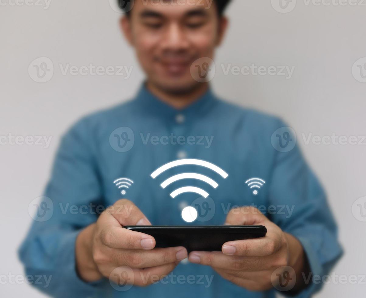 Young handsome wearing a light blue shirt turn use smarthphone connected to Wi-Fi technology for using smart home function. Technology business and modern lifestyle concept. photo