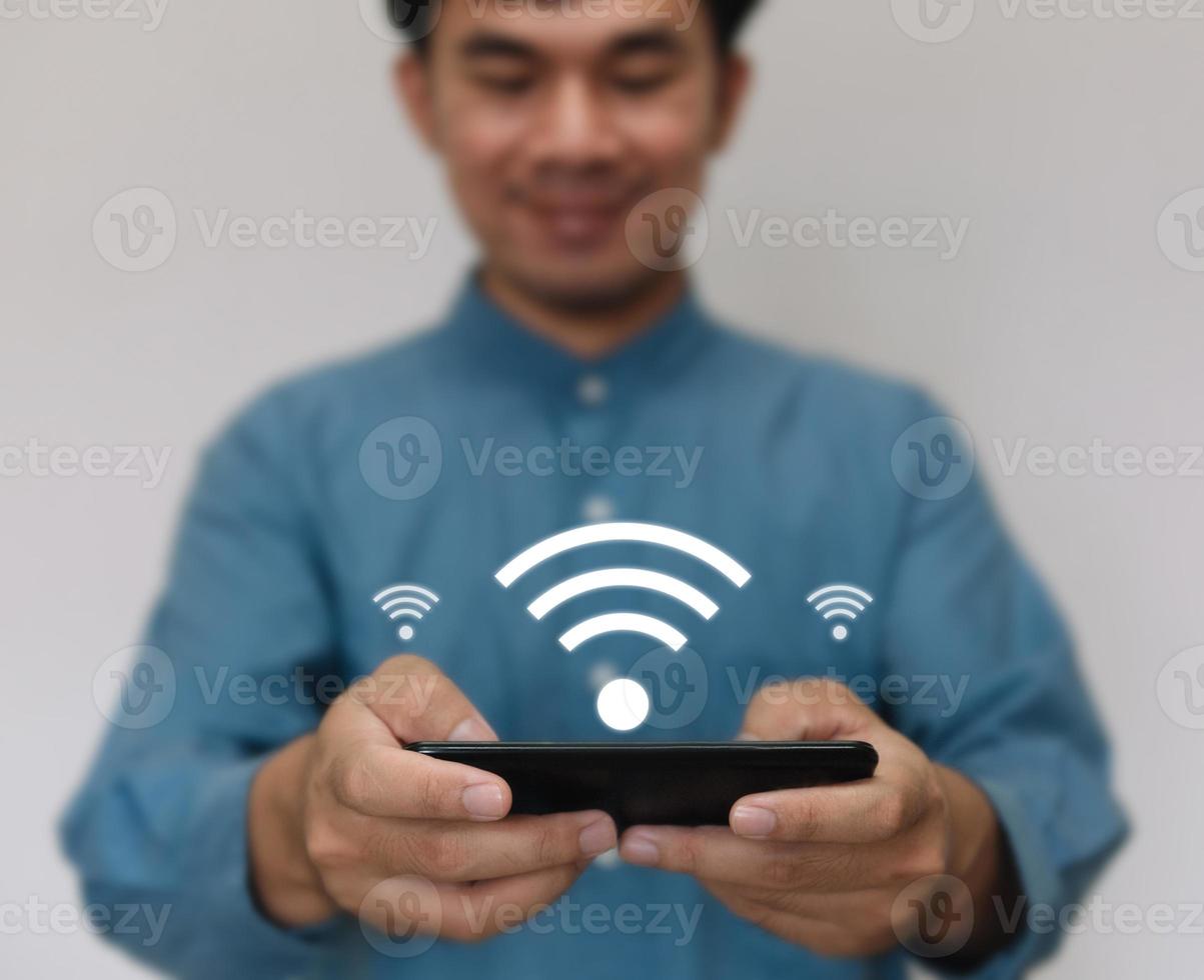 joven guapo con una camisa azul claro, use un teléfono inteligente conectado a la tecnología wi-fi para usar la función de hogar inteligente. negocio de tecnología y concepto de estilo de vida moderno. foto