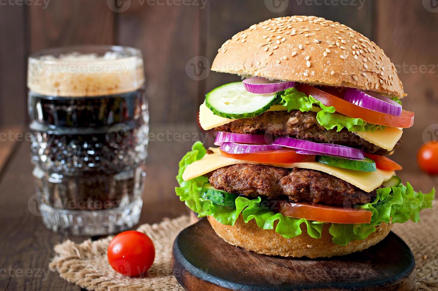 Gran jugosa hamburguesa con verduras y carne sobre un fondo de madera en estilo rústico foto