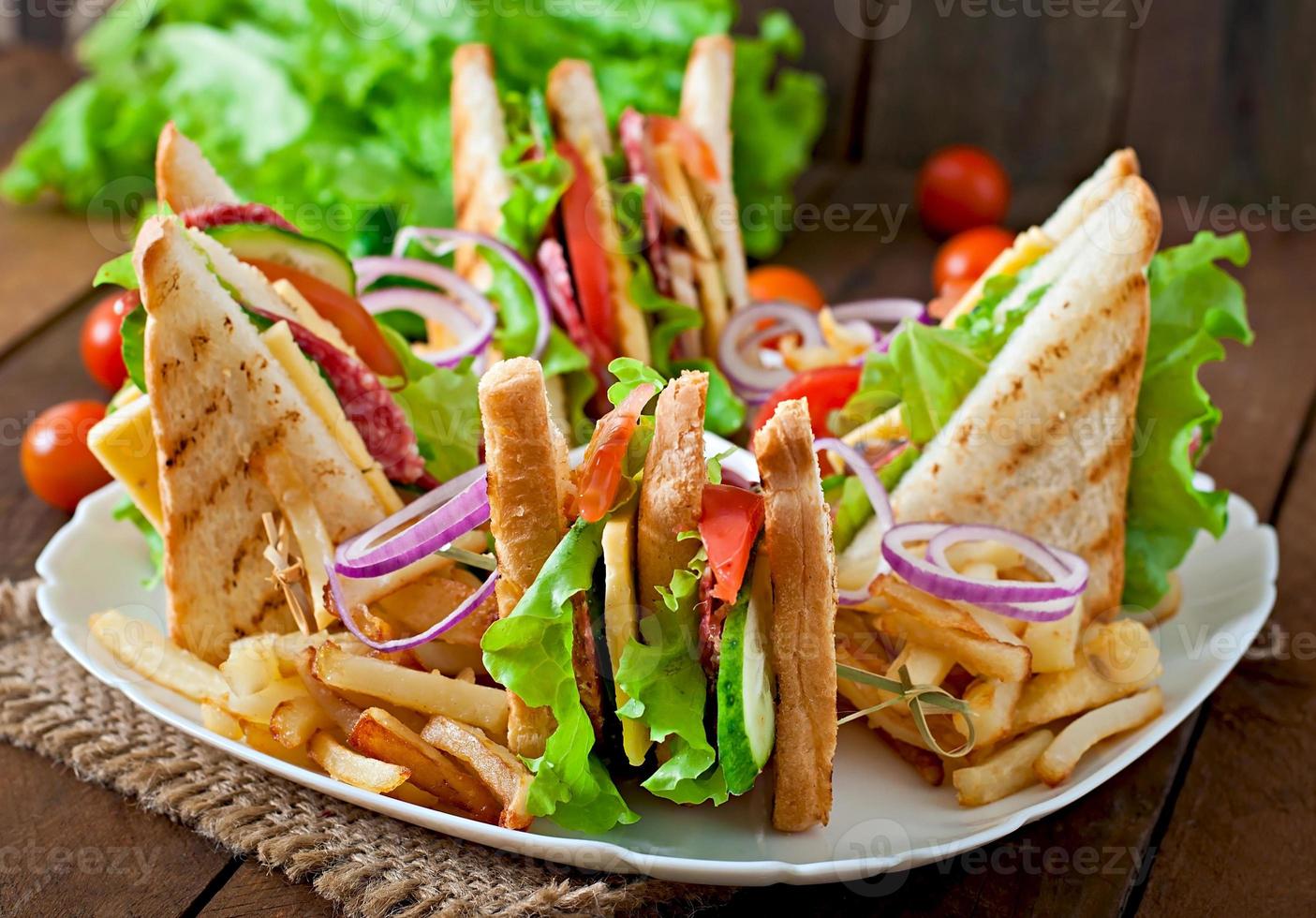 Club sandwich with cheese, cucumber, tomato, smoked meat and salami. Served with French fries. photo