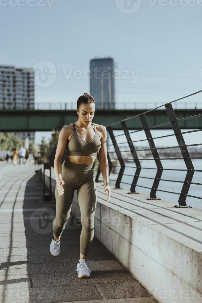 Young woman in sportswear stretching on a river promenade photo