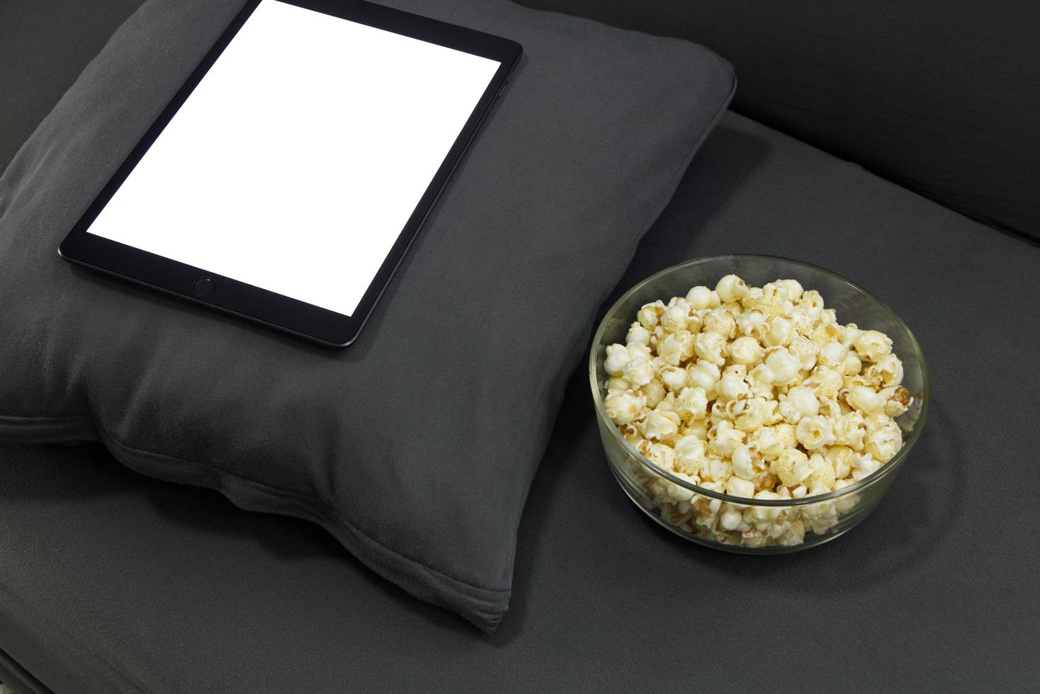 Glass cup with salted popcorn digital tablet in a gray armchair. photo
