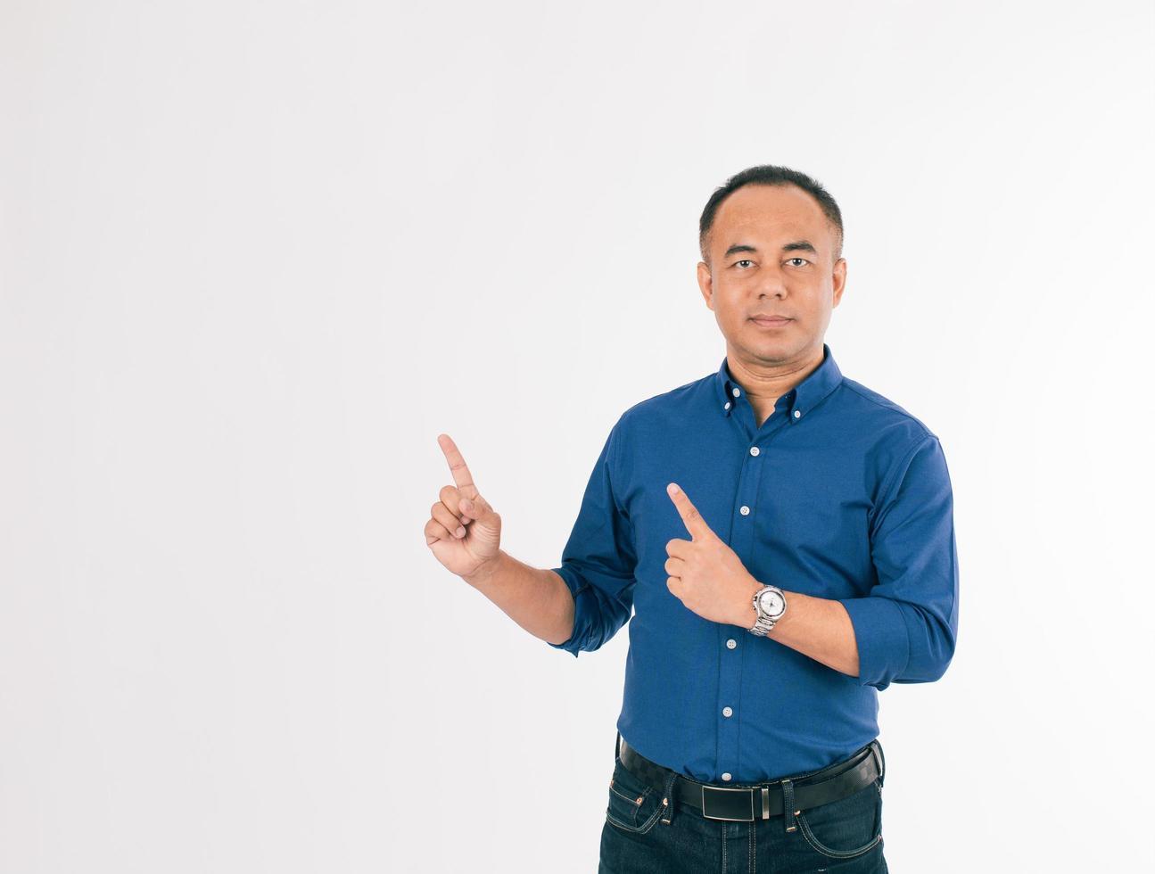 A self-confident senior Asian man in a blue business casual shirt standing and pointing fingers into the air with copy space. photo