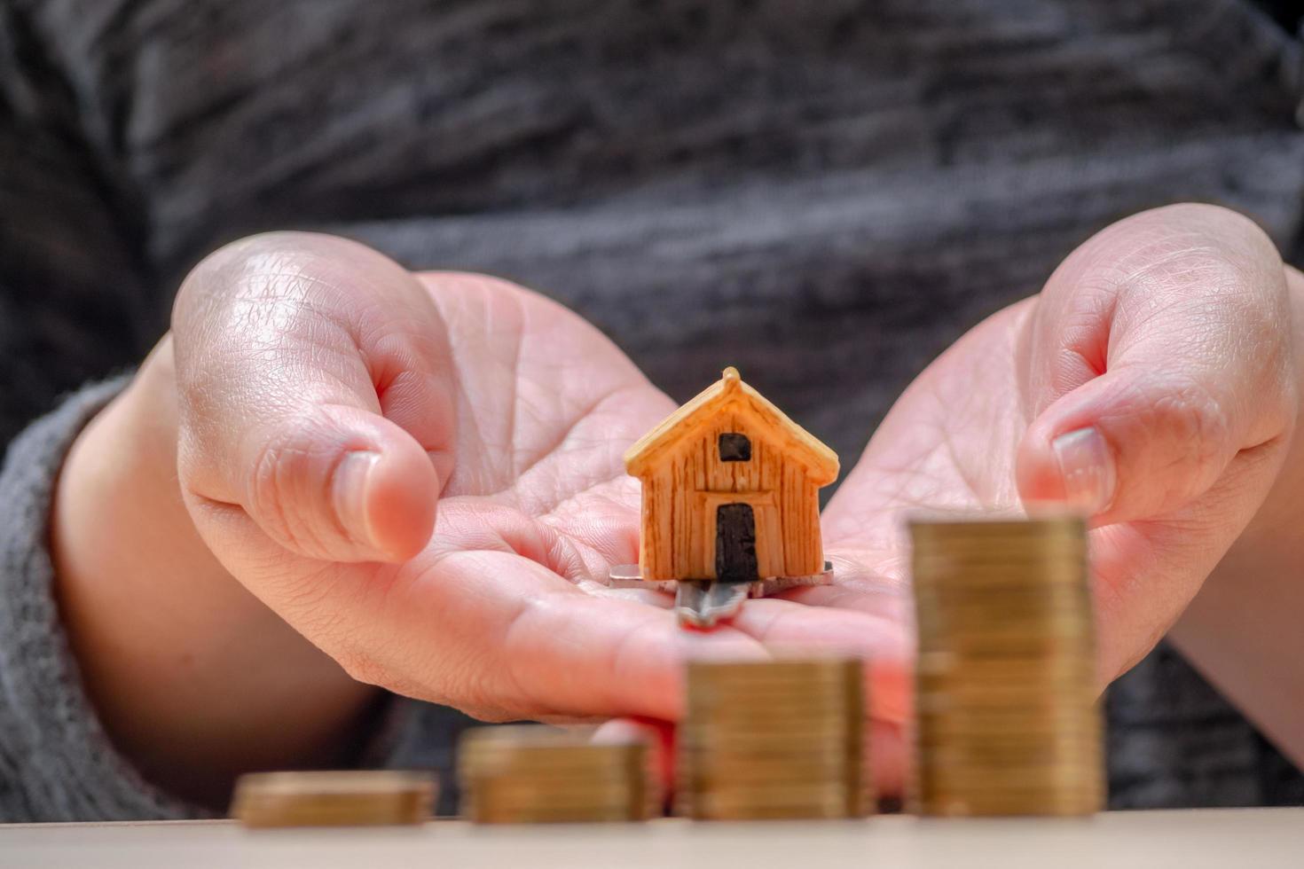 House or Home model and coins on hand with home key. Concept for loan, property ladder, financial, mortgage, real estate investment, taxes and bonus. photo