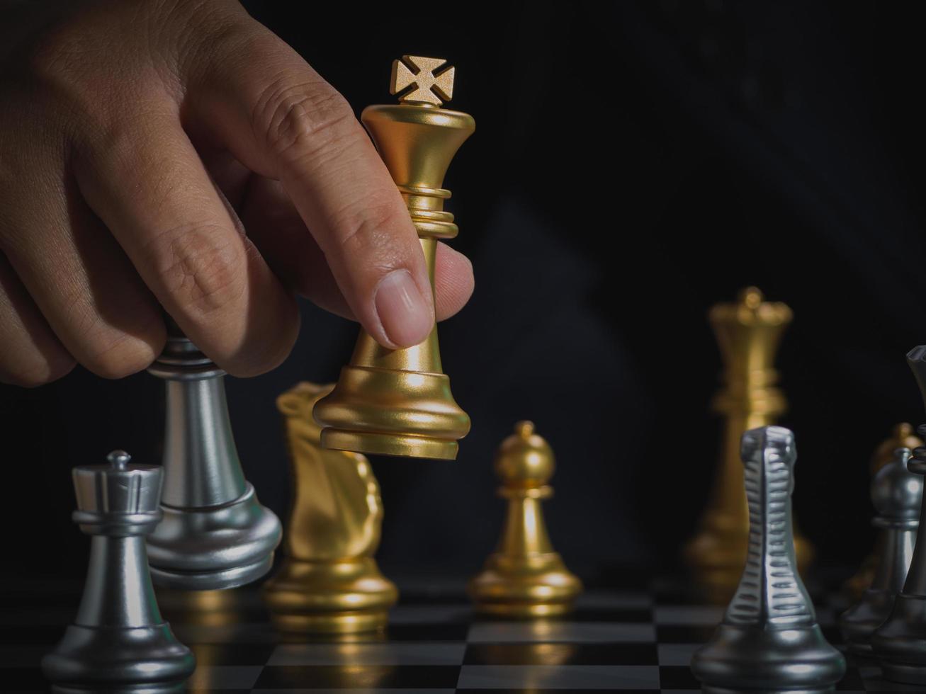 Hand of businessman holding gold king checkmate silver king on chess board to successfully in the competition. Management or leadership strategy and teamwork concept. photo