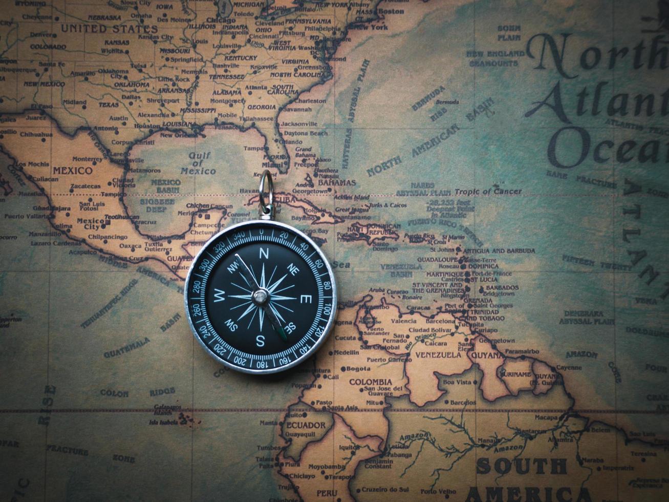 The compass is placed on the ancient or vintage world map between the United States of America and South America. Travel geography navigation concept background. photo