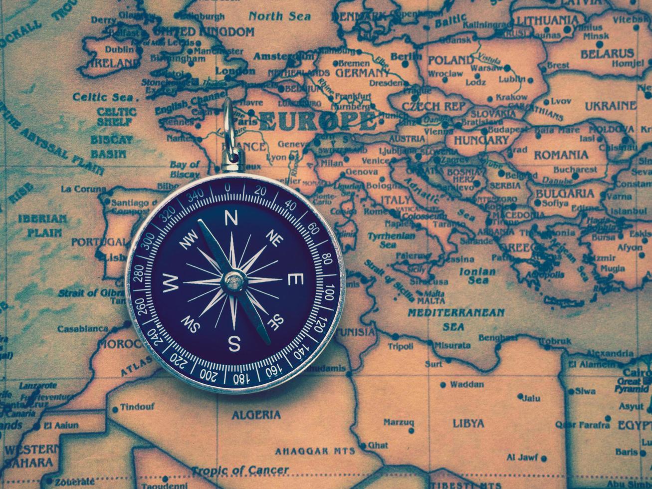 The compass is placed on the ancient or vintage world map between Europe continent and Africa continent. Travel geography navigation concept background. photo