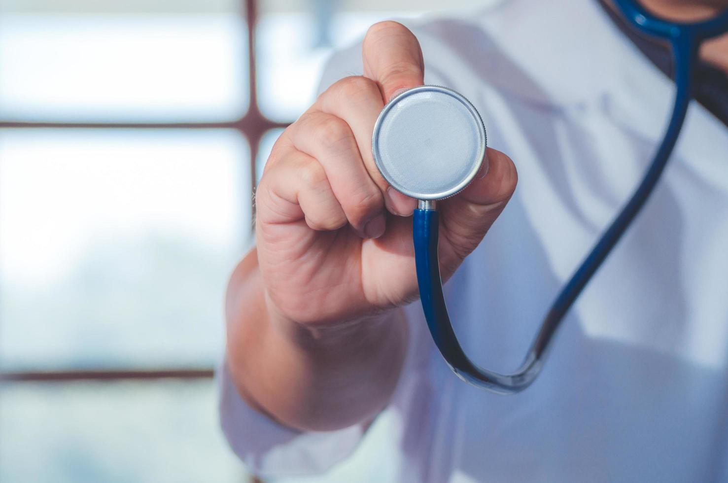 médico de medicina masculina mano sosteniendo estetoscopio contra el pecho en el fondo del hospital. médico listo para examinar al paciente. concepto de atención médica y del paciente. foto