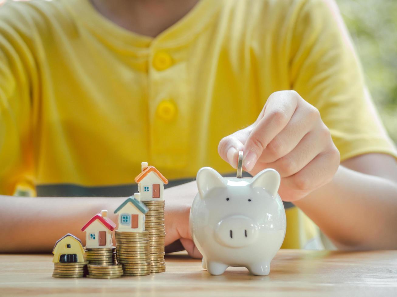 un niño asiático con monedas deja caer un contenedor ahorrando dinero para ahorrar dinero, invertir para el futuro y comprar una casa. concepto de préstamo, escalera de propiedad, inversión financiera, inmobiliaria y bonificación. foto