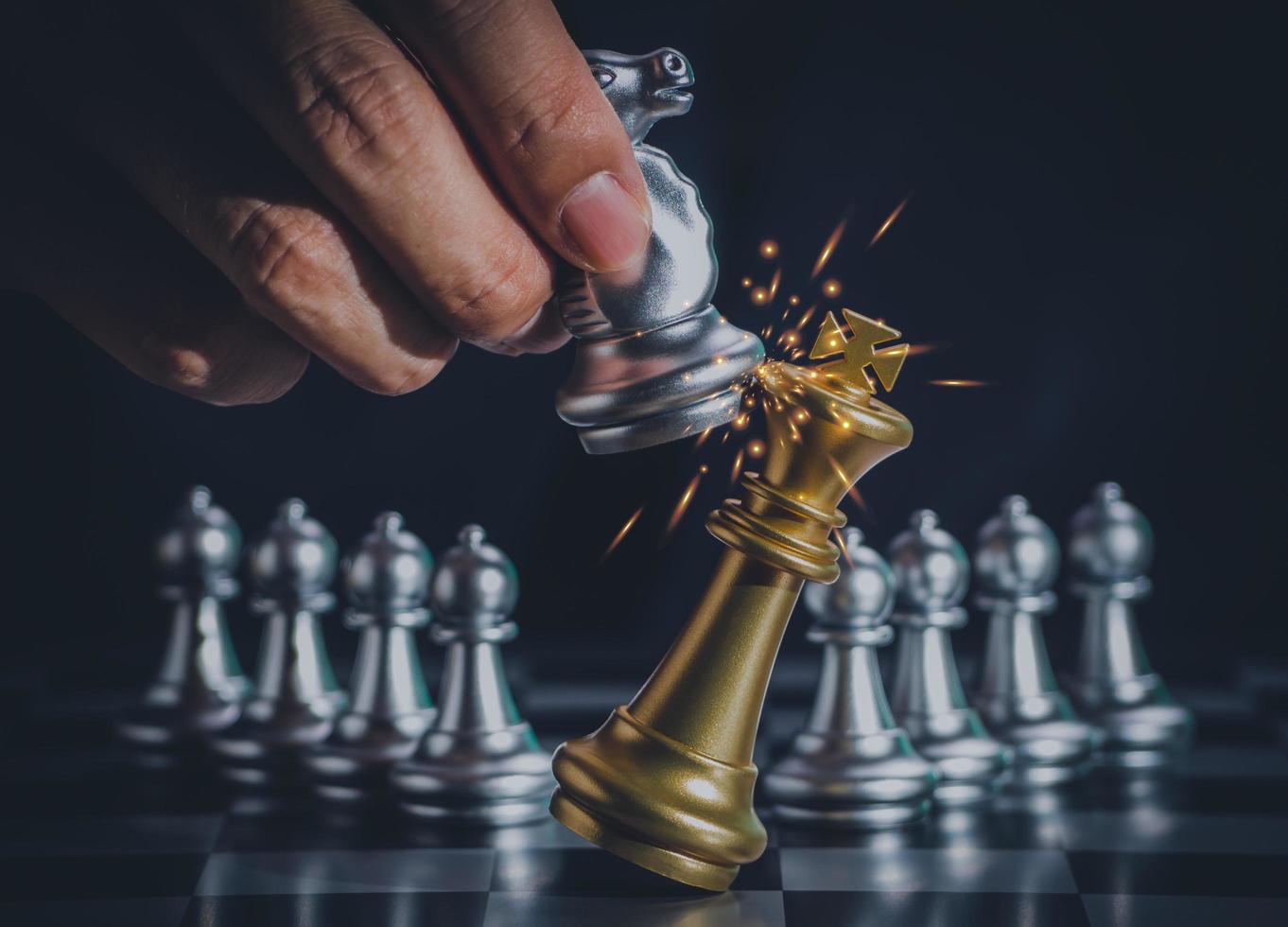 Hand businessman moving the silver knight chess fighting gold king with fire sparks chess on chess board to successfully in the competition. Management or leadership strategy and teamwork concept. photo