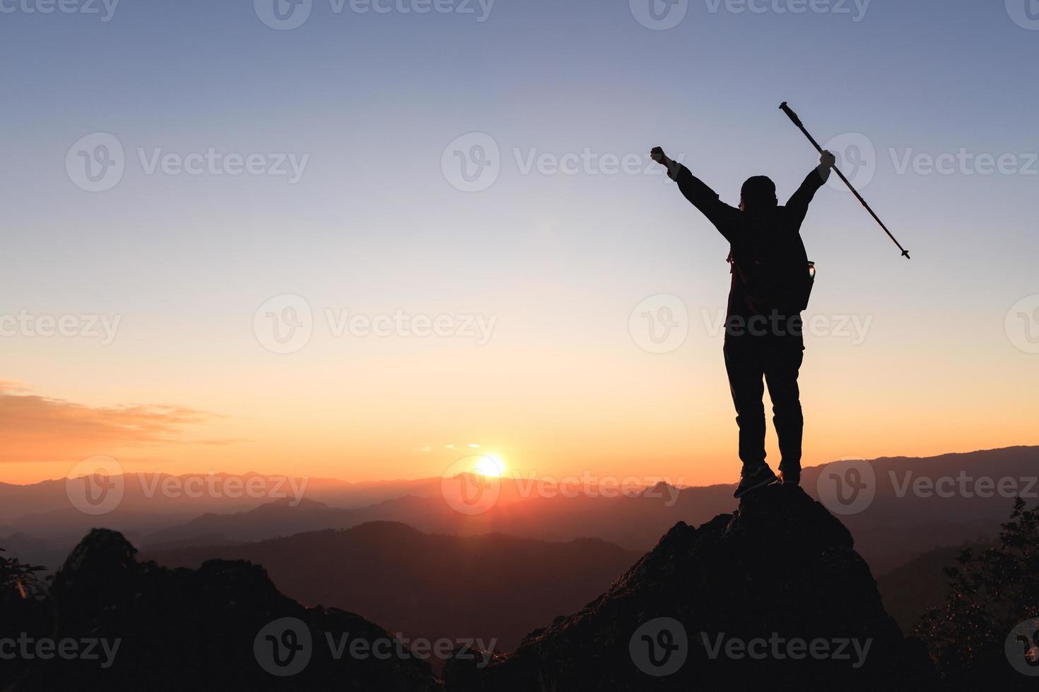 Silhouette of hiker standing on top of hill and enjoying sunrise over the valley.  The man thank God on the mountain and success photo