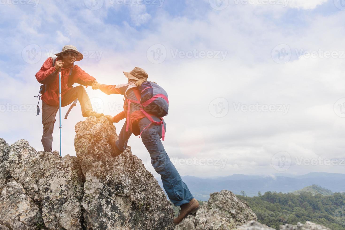 equipo de escaladores, hombres y mujeres, se ayudan unos a otros en la cima de la montaña, escalando caminatas juntos, jóvenes turistas con mochilas, foto