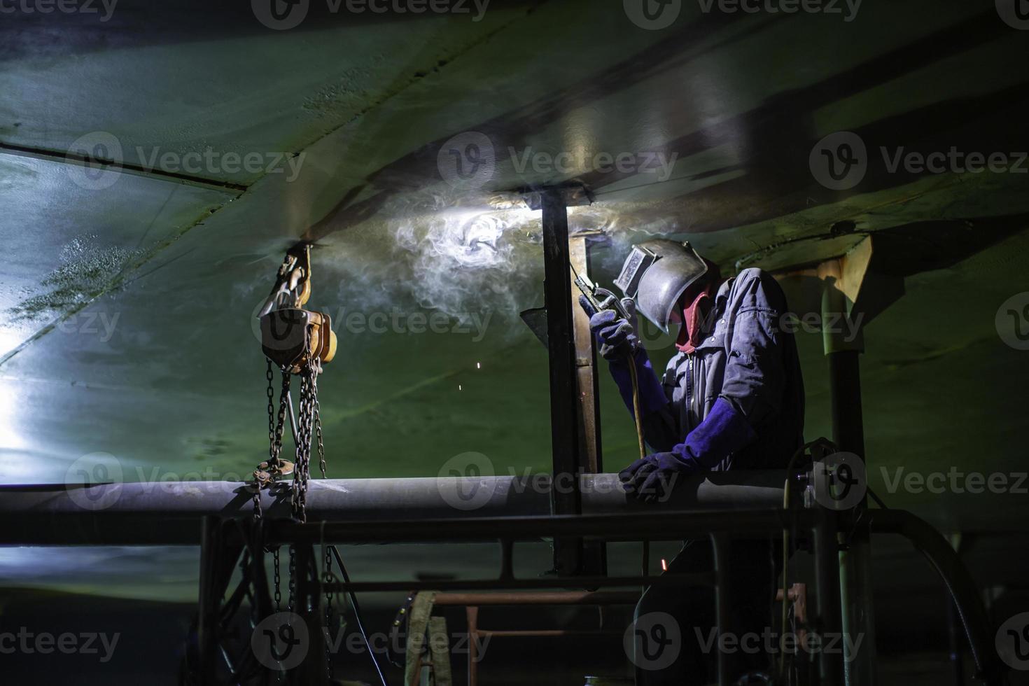 El arco de metal del trabajador masculino de soldadura es parte de la construcción de tuberías de la boquilla del tanque de maquinaria aceite del tanque dentro de espacios confinados. foto