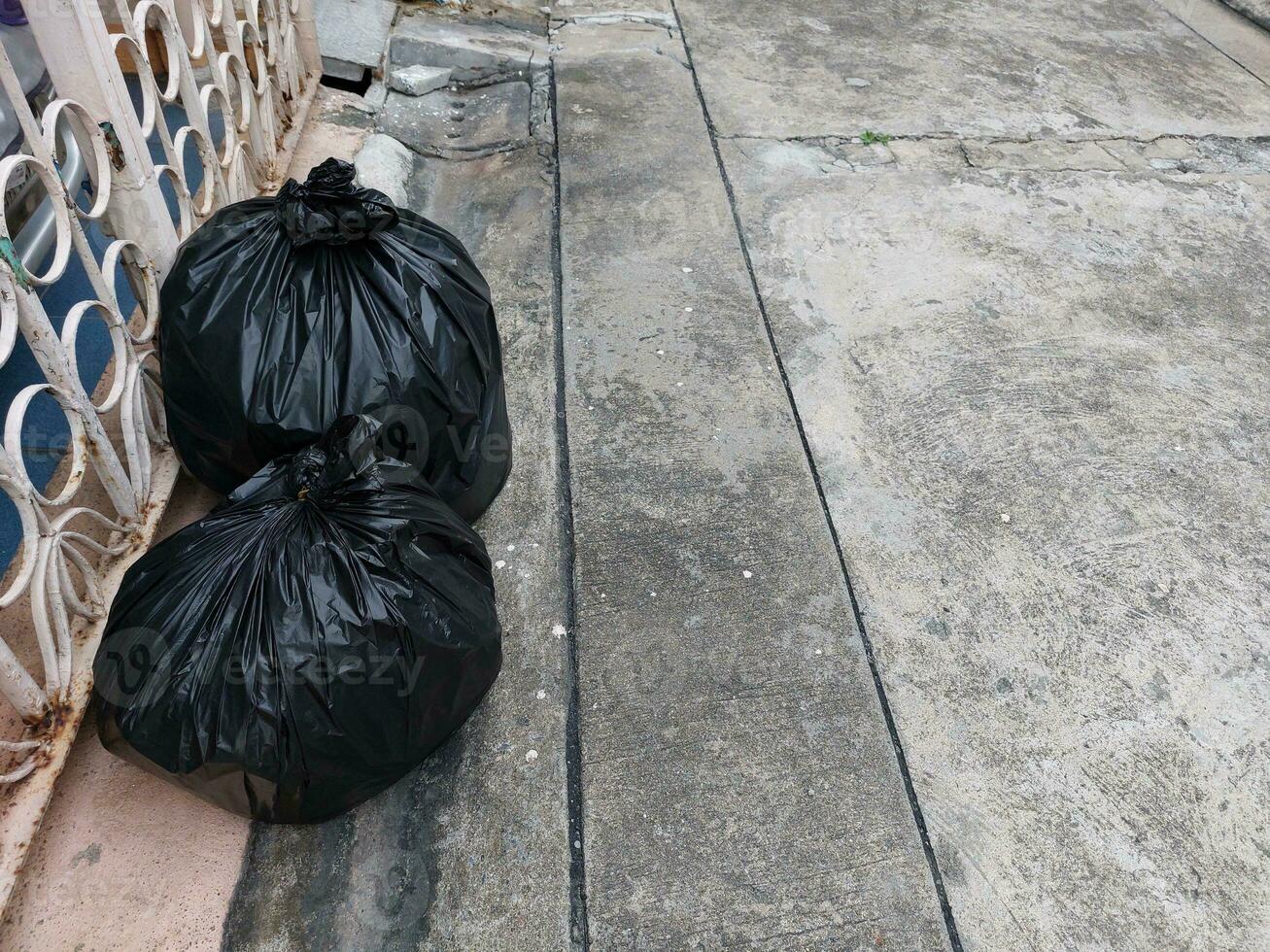 Two black trash bags were placed on the left side of the fence on the village road. photo