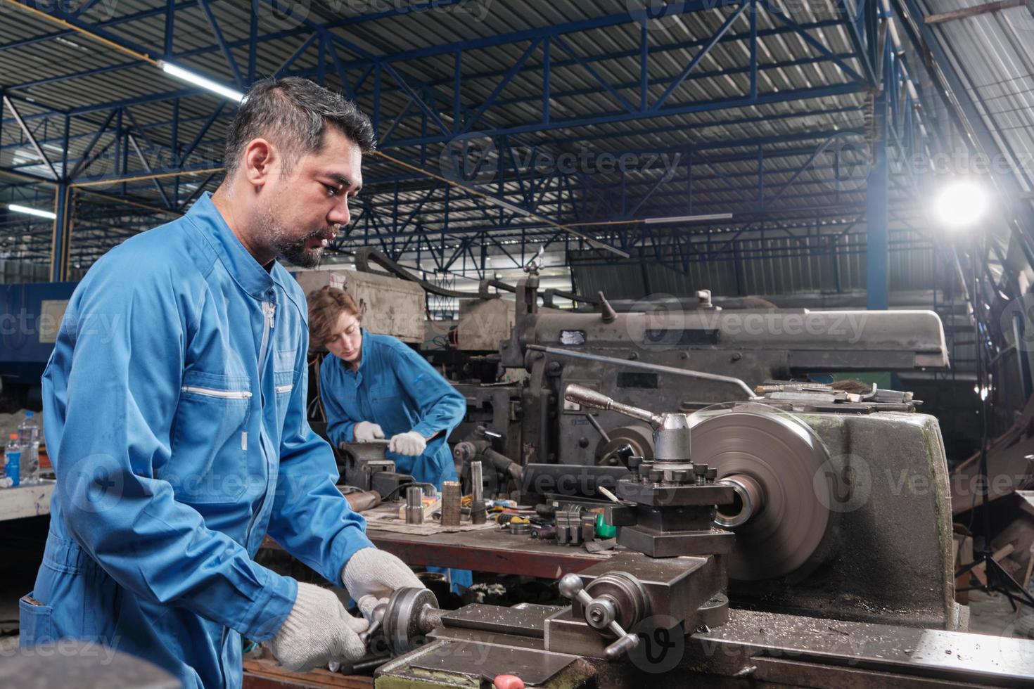El equipo profesional de la industria, dos trabajadores con uniformes de seguridad y un socio de ingenieros trabajaron con herramientas de metalurgia, tornos mecánicos y talleres de repuestos en la fábrica de fabricación de acero. foto