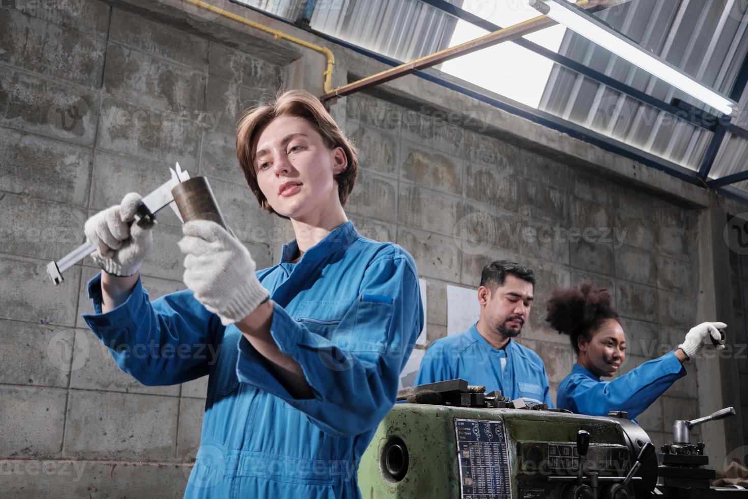 Young Caucasian female industry worker works with metalwork precision tools, lathe machines, and spare parts workshop with multiracial team in manufacturing factory, professional mechanical engineers. photo