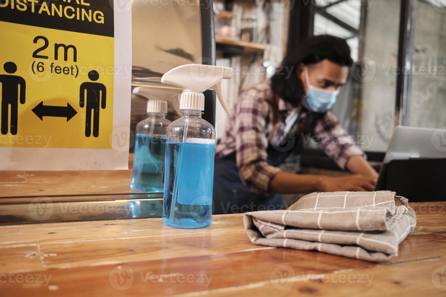 Alcohol sanitizer for healthy protection in a cafe, Asian male barista in face mask use laptop, waiting for coffee order in COVID19 pandemic quarantine, the economic impact for small business startup. photo