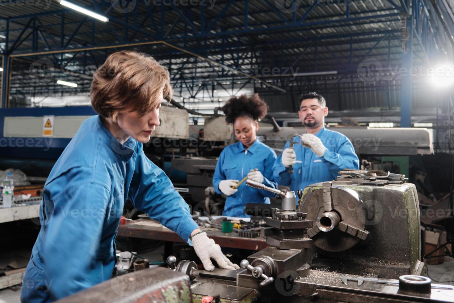 Young Caucasian female industry worker works with metalwork precision tools, lathe machines, and spare parts workshop with multiracial team in manufacturing factory, professional mechanical engineers. photo