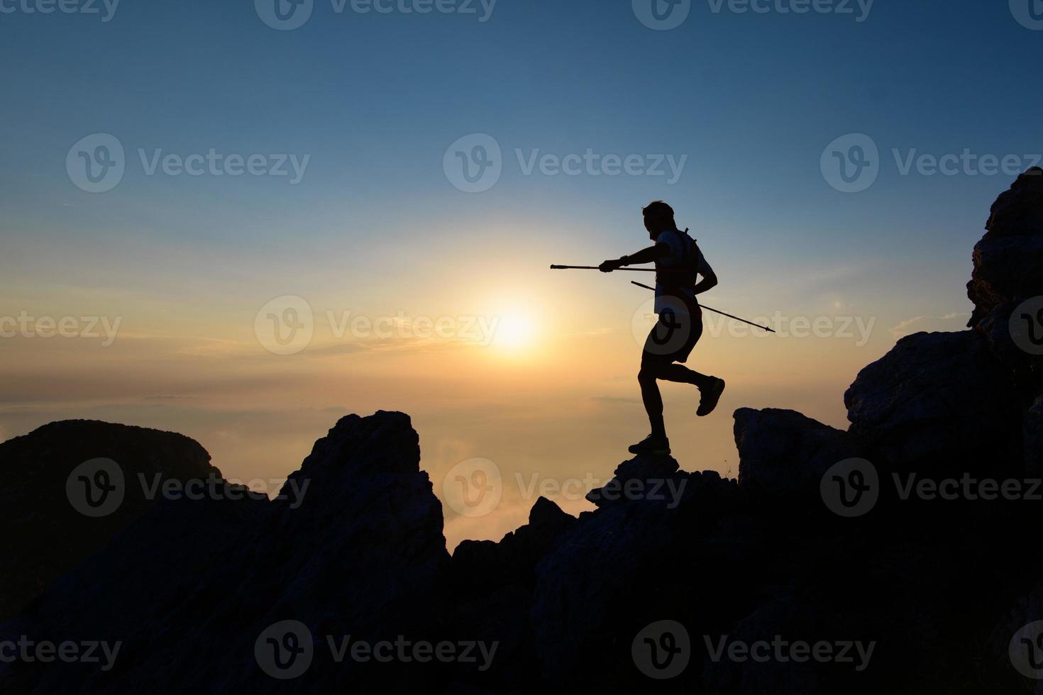 Athlete skyrunner in silhouette on the downhill rocks photo