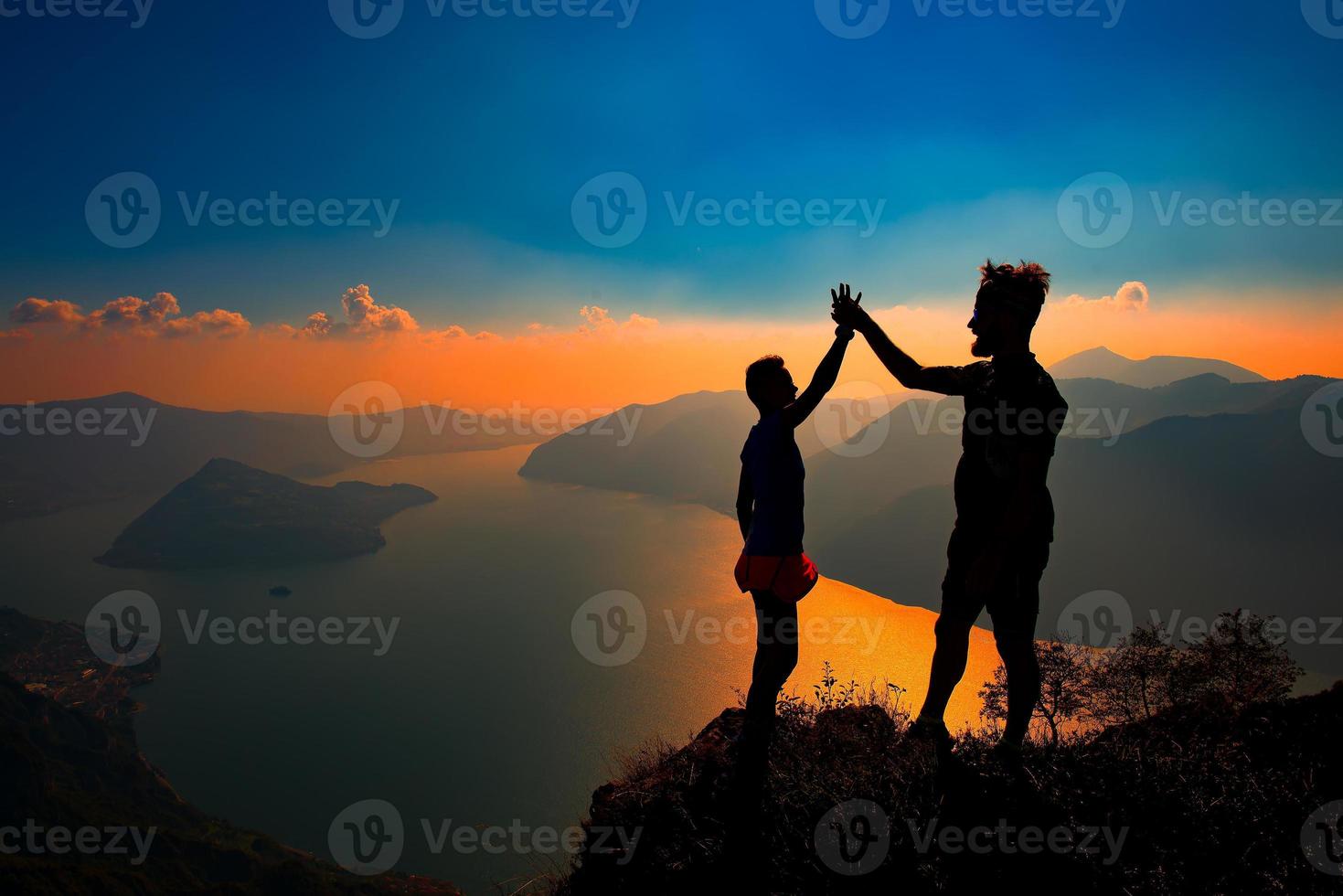 A pair shake hands in victory on top of a mountain photo