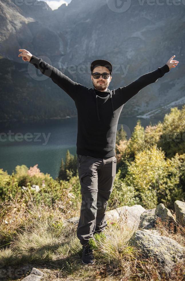 joven turista con una gorra con las manos arriba en la cima de las montañas foto