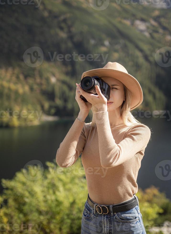 Photographer tourist traveler standing on green top on mountain holding in hands digital photo camera