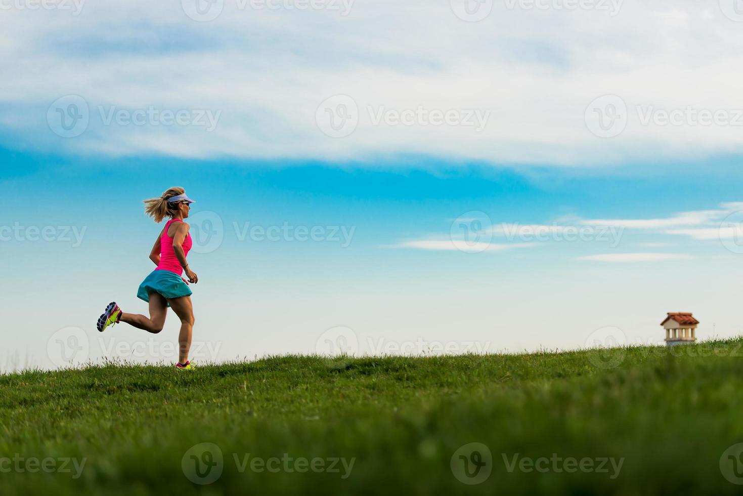Blonde girl athlete runs in a green meadow in the hills photo