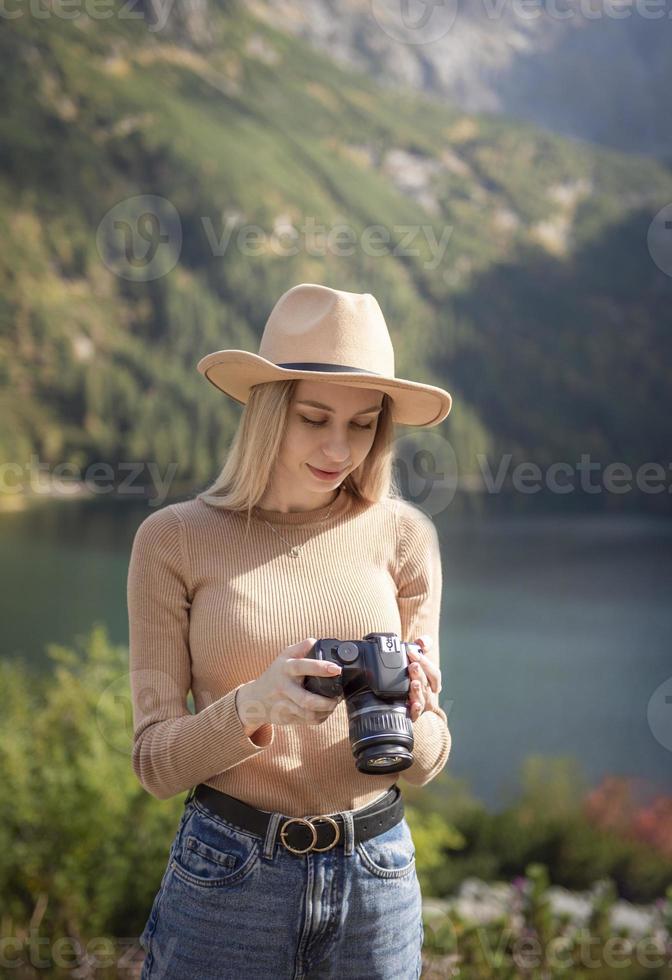 Photographer tourist traveler standing on green top on mountain holding in hands digital photo camera
