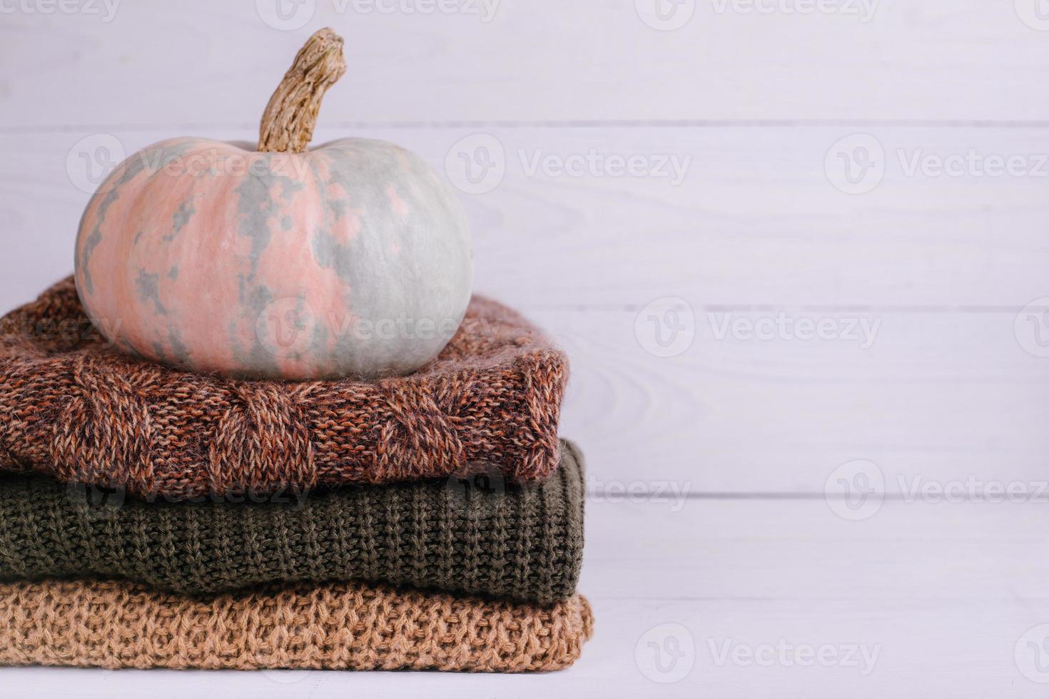 A pile of warm sweaters on white wooden background with pumpkin, knitwear photo