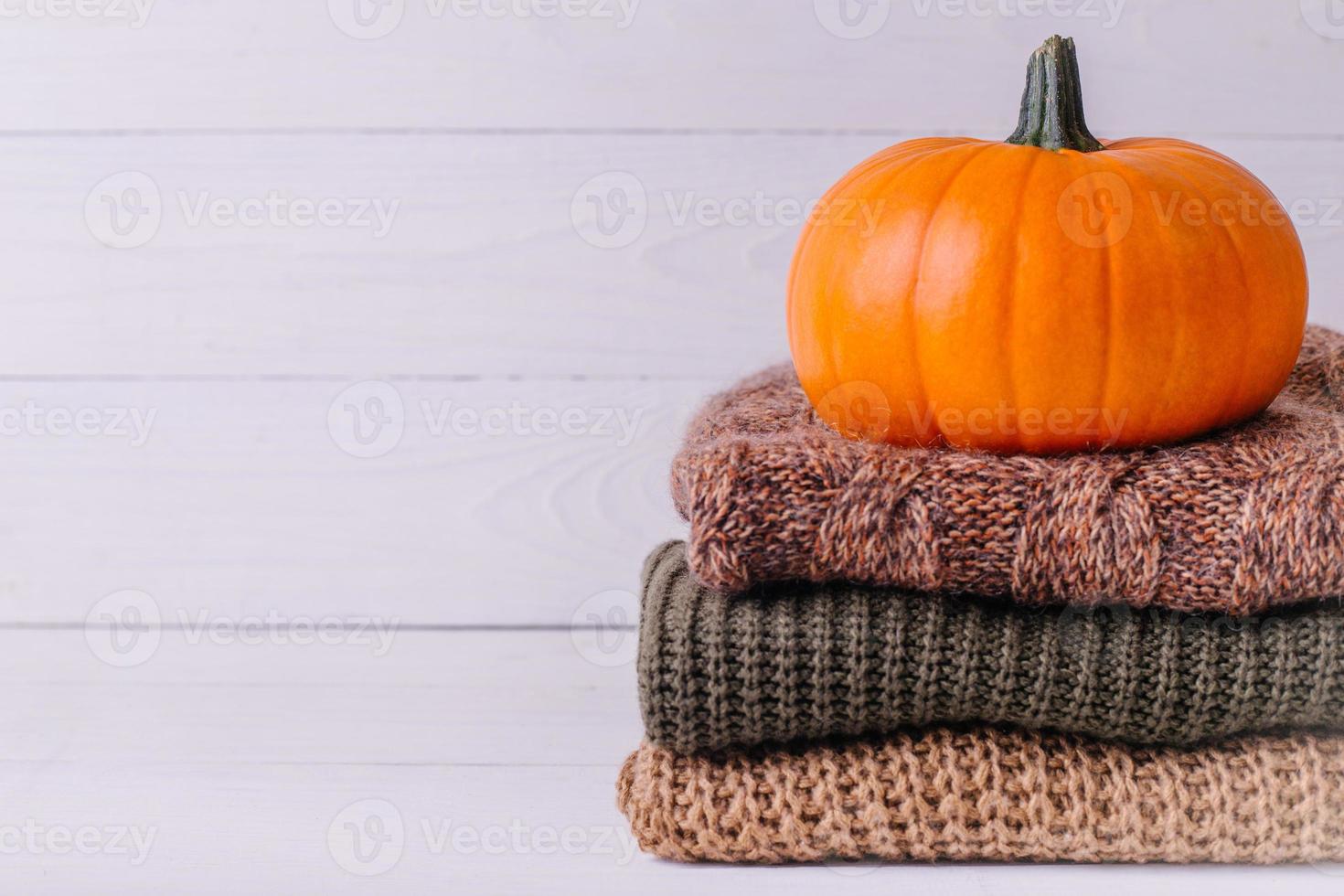 un montón de suéteres cálidos sobre fondo blanco de madera con calabaza, géneros de punto foto