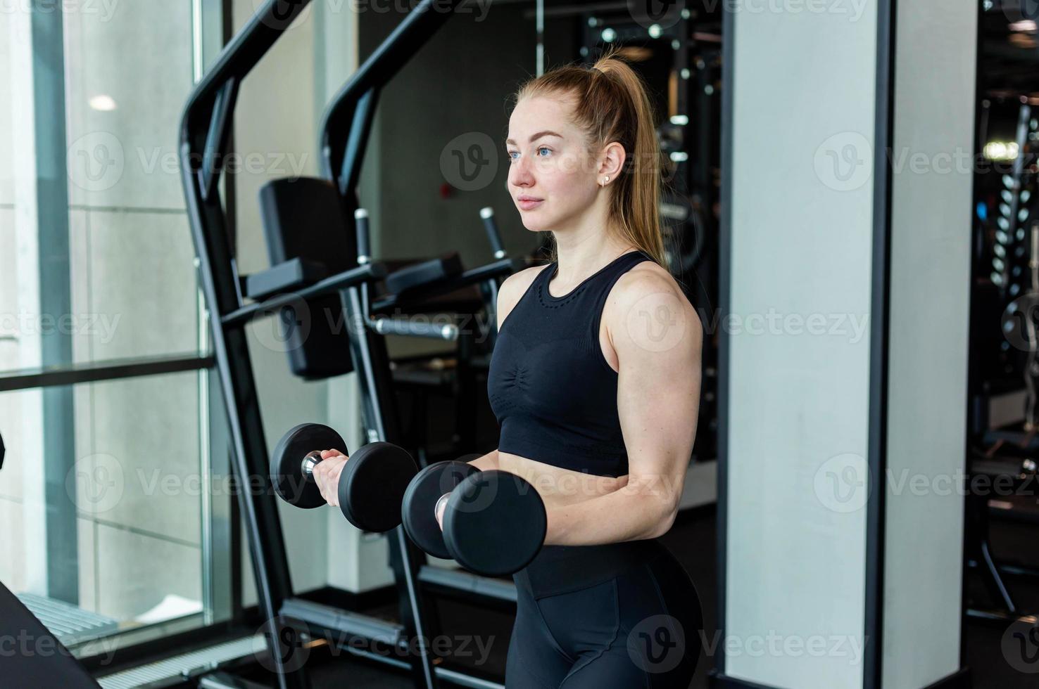 A young girl in black sportswear is engaged in the gym with dumbbells. Fitness club concept. photo