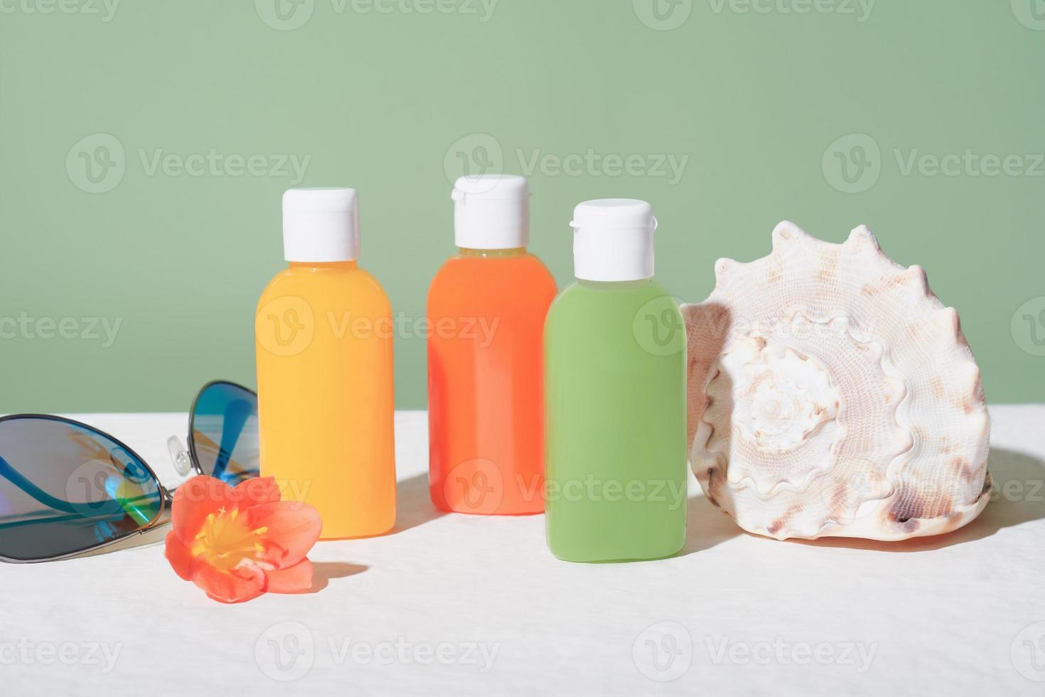 juego de botellas cosméticas de viaje y conchas marinas y gafas de sol. concepto de vacaciones tropicales. kit de autocuidado. champú, gel de baño, acondicionador en minibotellas. foto