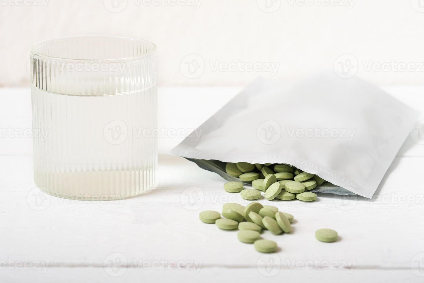 pastillas de hierba de cebada en una mesa junto a un vaso de agua. Tabletas de espirulina y chlorella para desintoxicación y suplemento metabólico. superalimento vegano crudo. foto