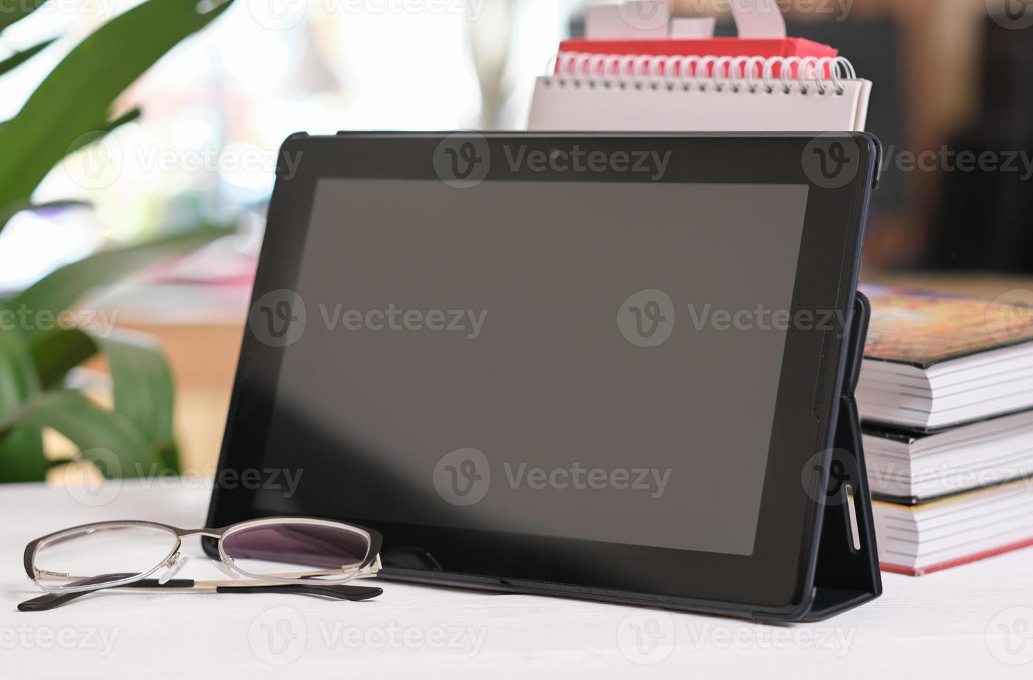 digital tablet on a desk with eyeglasses and books in a living room. education, home learning, online study concept. photo
