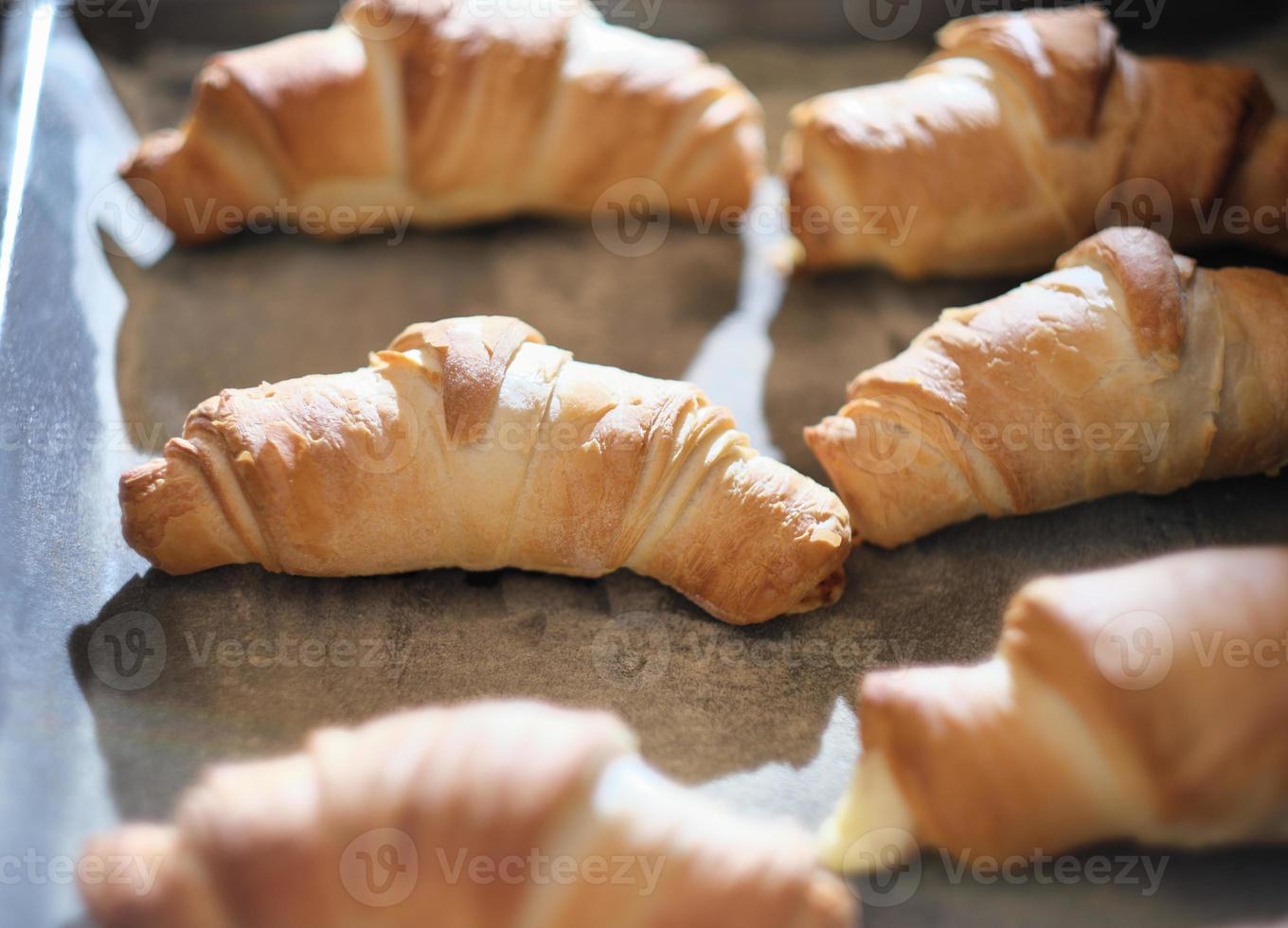 croissants al horno en una bandeja para hornear. panecillos dulces horneados en horno caliente. el proceso de hacer bagels de cuajada o croissants franceses. foto