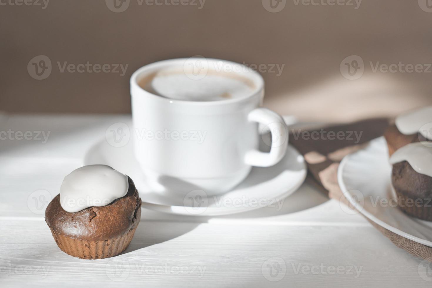 taza de café con leche y cupcakes recién horneados con glaseado. muffins de chocolate horneados en casa por la mañana. luz natural. foto