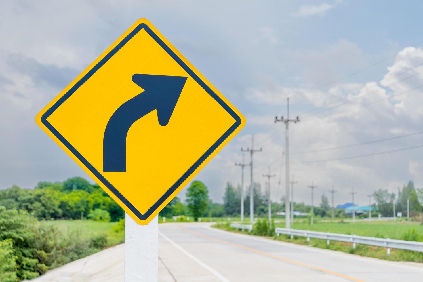 The new symbol reflective yellow right turn sign has a black arrow inside the frame located on the side of the country road. safety information transport roadside photo