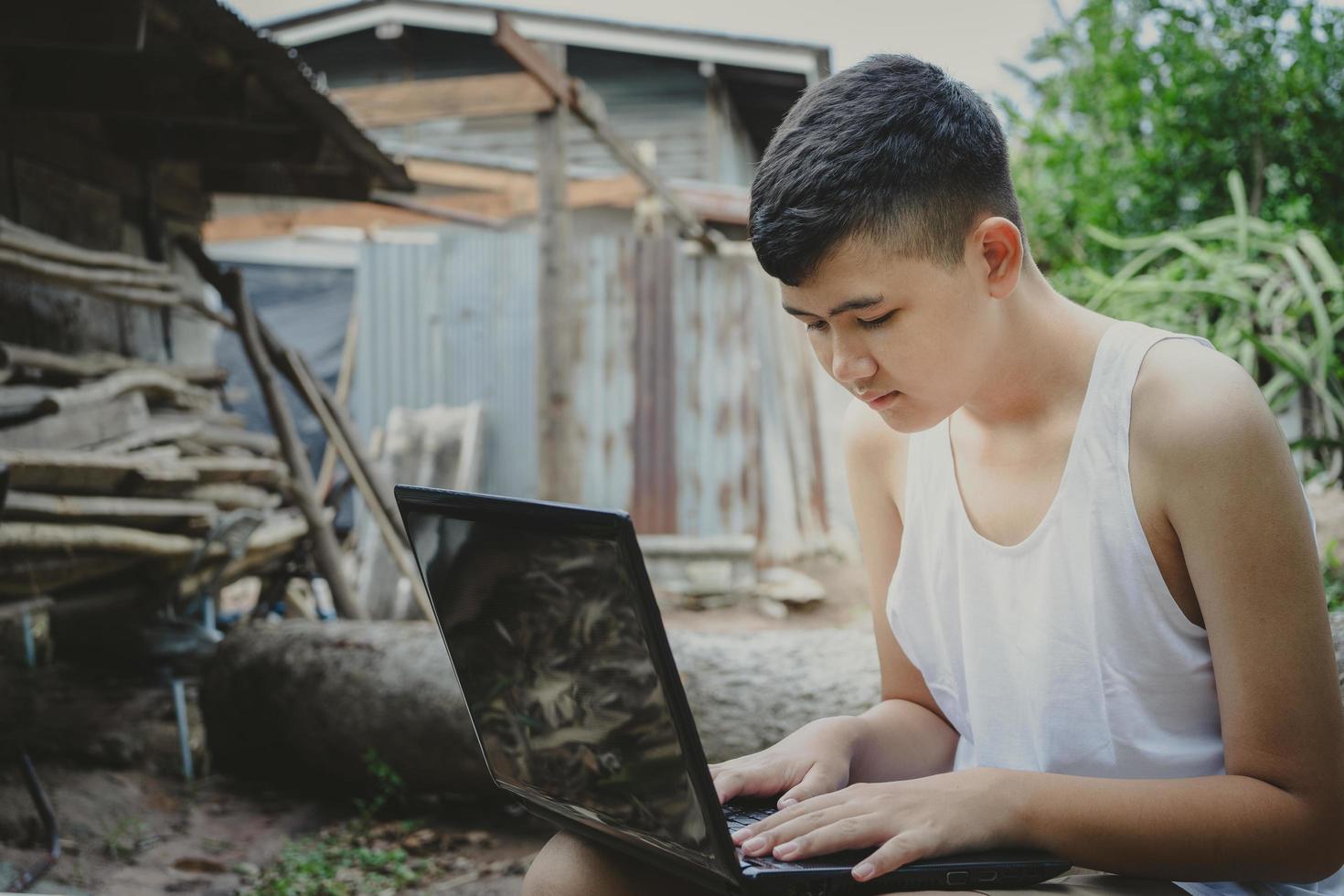 niño asiático estudiando en línea con una computadora portátil en su escritorio en el campo, aprendiendo con un maestro en casa, educación en el hogar a distancia, aprender en línea en Internet rural, poca falta de equipo educativo foto