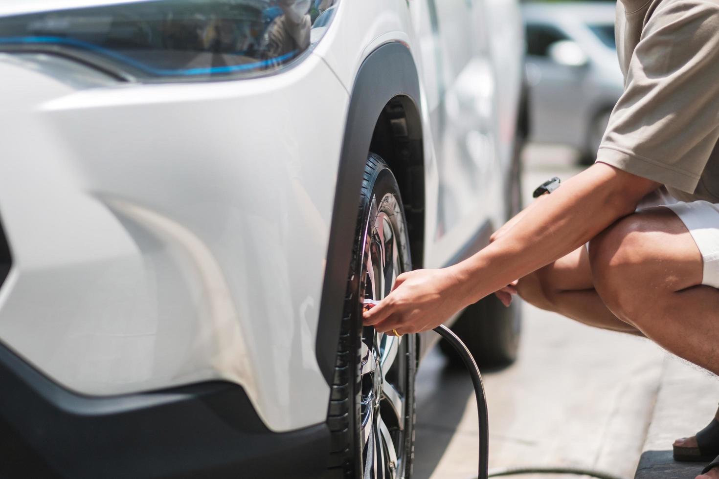 man driver hand inflating tires of vehicle, removing tire valve nitrogen cap for checking air pressure and filling air on car wheel at gas station. self service, maintenance and safety photo