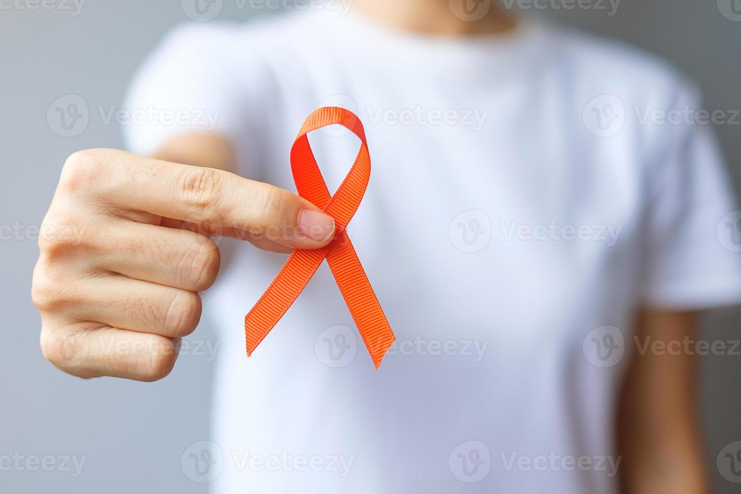 hand holding Orange Ribbon for Leukemia, Kidney cancer day, world Multiple Sclerosis, CRPS, Self Injury Awareness month. Healthcare and word cancer day concept photo