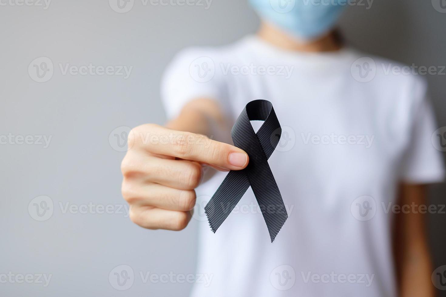 Woman holding black Ribbon for Melanoma and skin cancer, Vaccine injury awareness month, grief and rest in peace. Healthcare and Racist concept photo