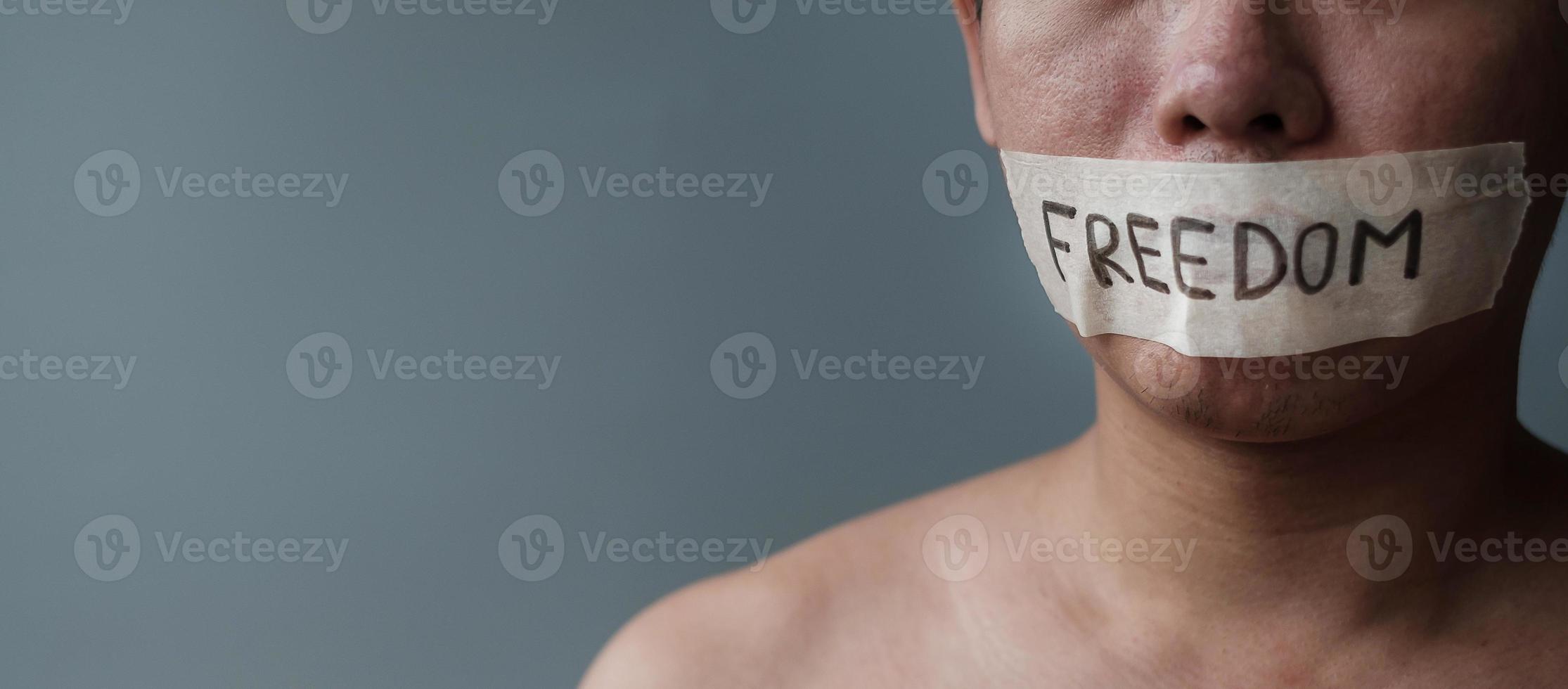 Man with mouth sealed in adhesive tape with Freedom message. Free of speech, freedom of press, Human rights, Protest dictatorship, democracy, liberty, equality and fraternity concepts photo