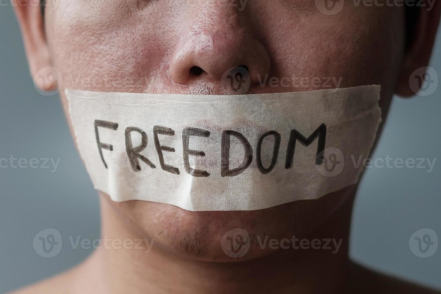 Man with mouth sealed in adhesive tape with Freedom message. Free of speech, freedom of press, Human rights, Protest dictatorship, democracy, liberty, equality and fraternity concepts photo