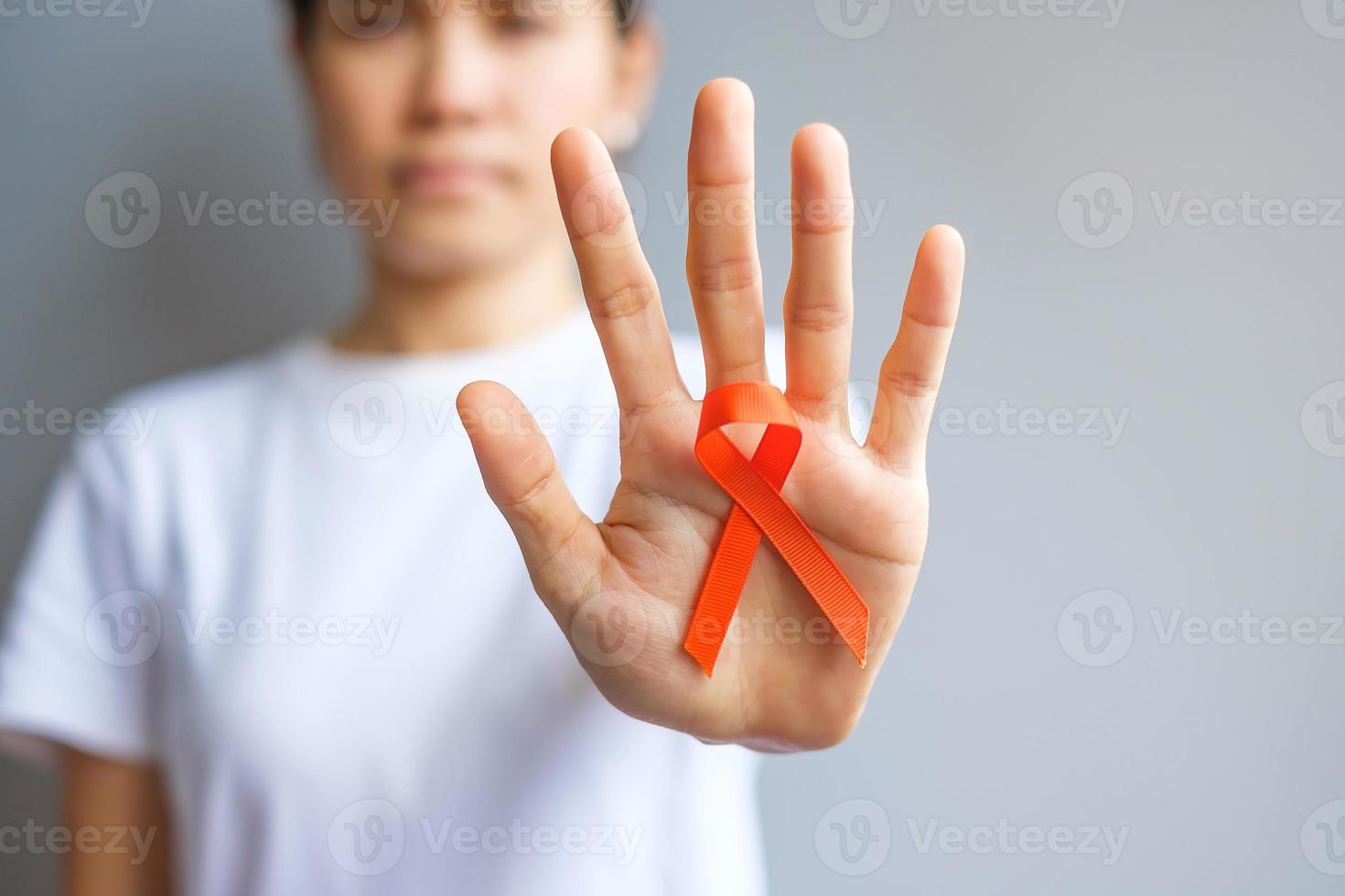 mano sosteniendo cinta naranja para leucemia, día del cáncer de riñón, esclerosis múltiple mundial, crps, mes de concientización sobre autolesiones. cuidado de la salud y el concepto del día del cáncer de palabra foto