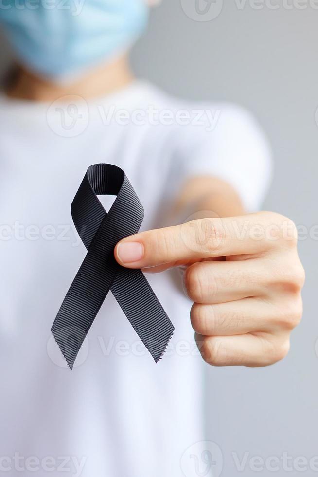 Woman holding black Ribbon for Melanoma and skin cancer, Vaccine injury awareness month, grief and rest in peace. Healthcare and Racist concept photo