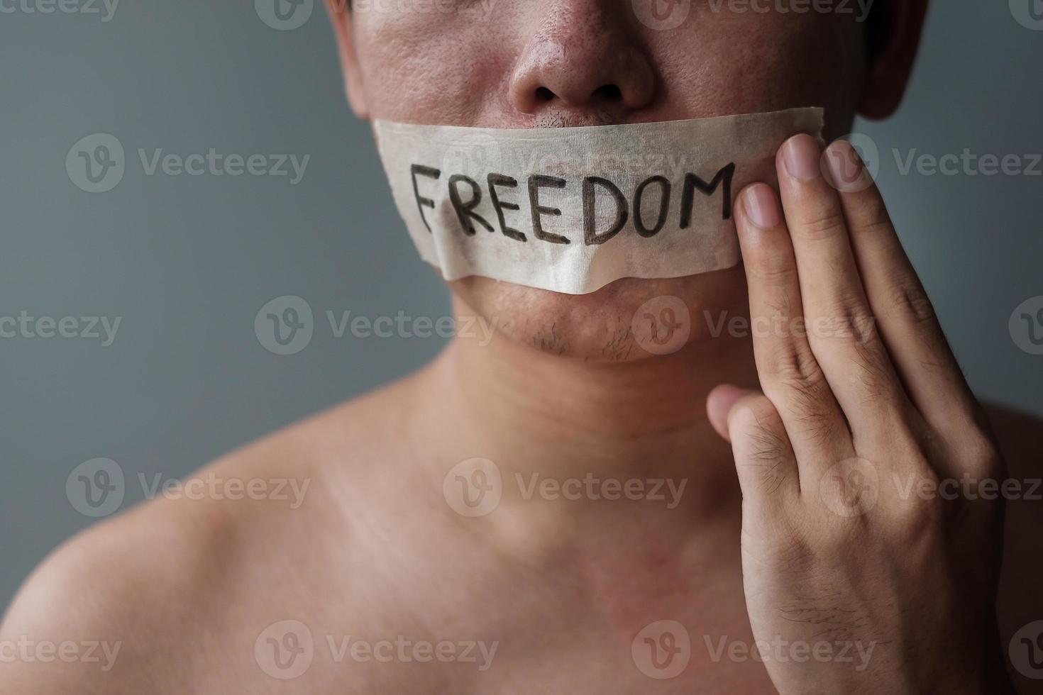 Man show three fingers  with mouth sealed in adhesive tape with Freedom message. Free of speech, Human rights, Protest dictatorship, democracy, liberty, equality and fraternity concepts photo