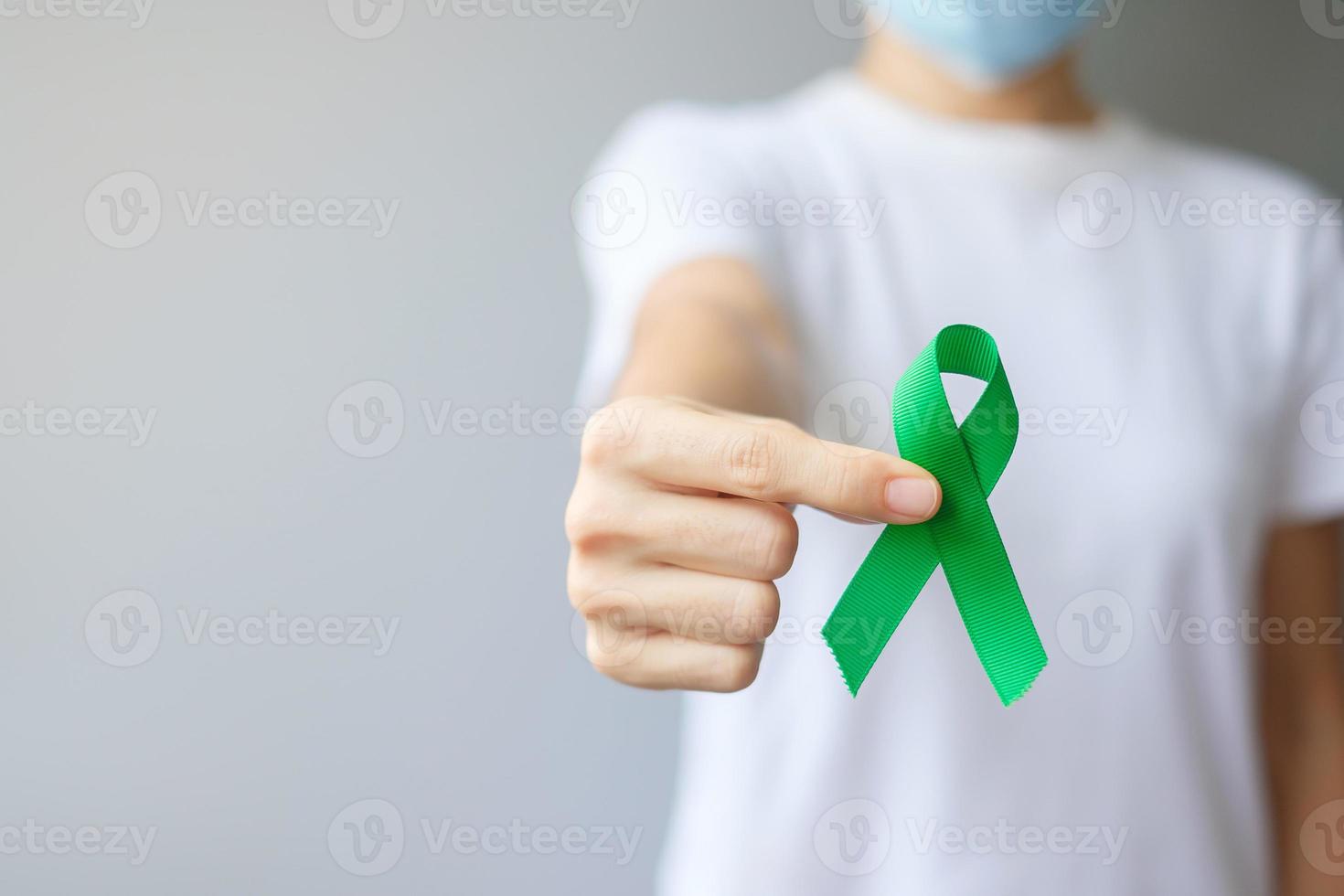 Hand holding green Ribbon for Liver, Gallbladders, bile duct, cervical, kidney Cancer and Lymphoma Awareness month. Healthcare and world cancer day concept photo